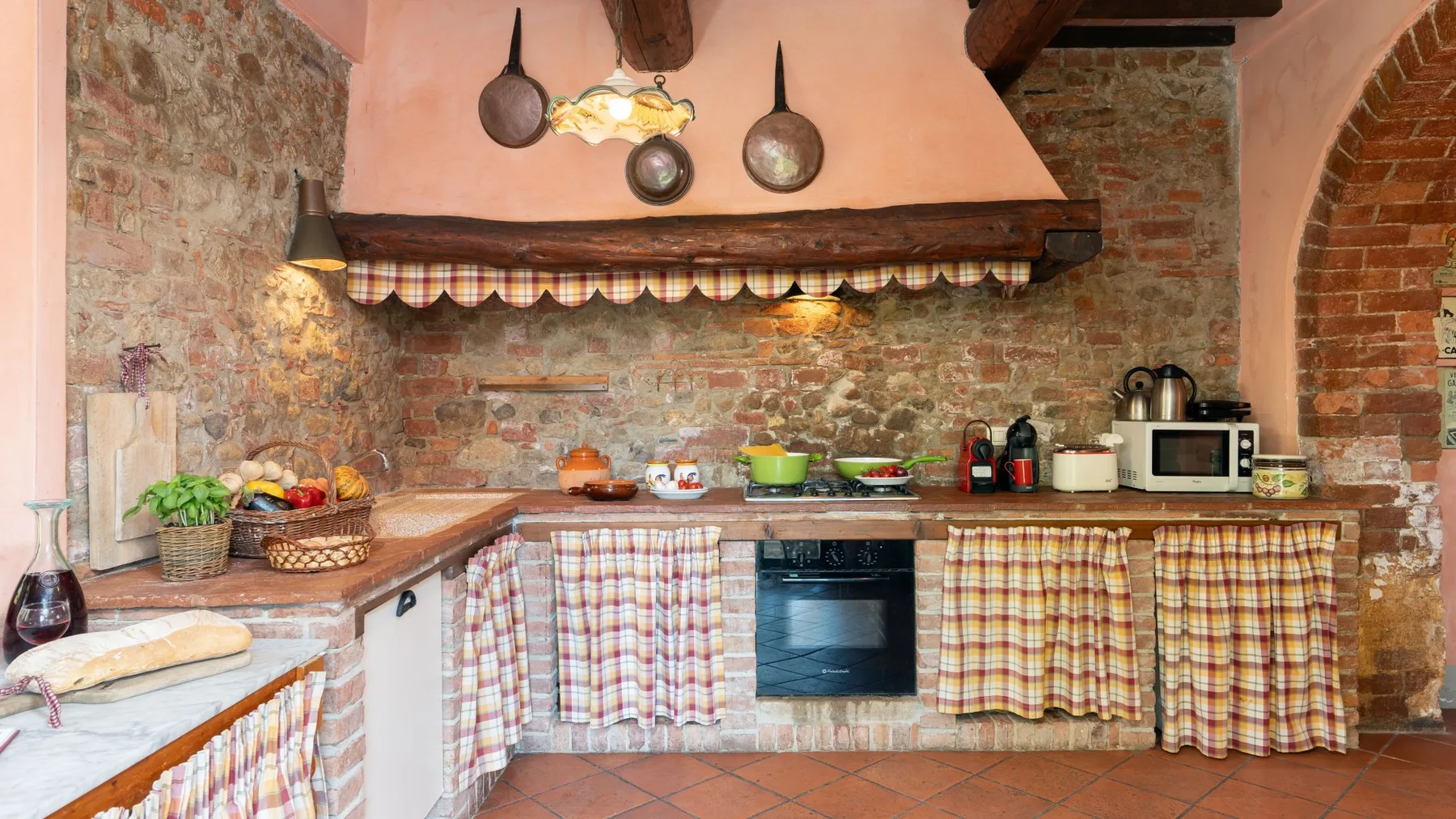 Una cocina rústica con paredes de ladrillo visto, una cocina y cortinas a cuadros.