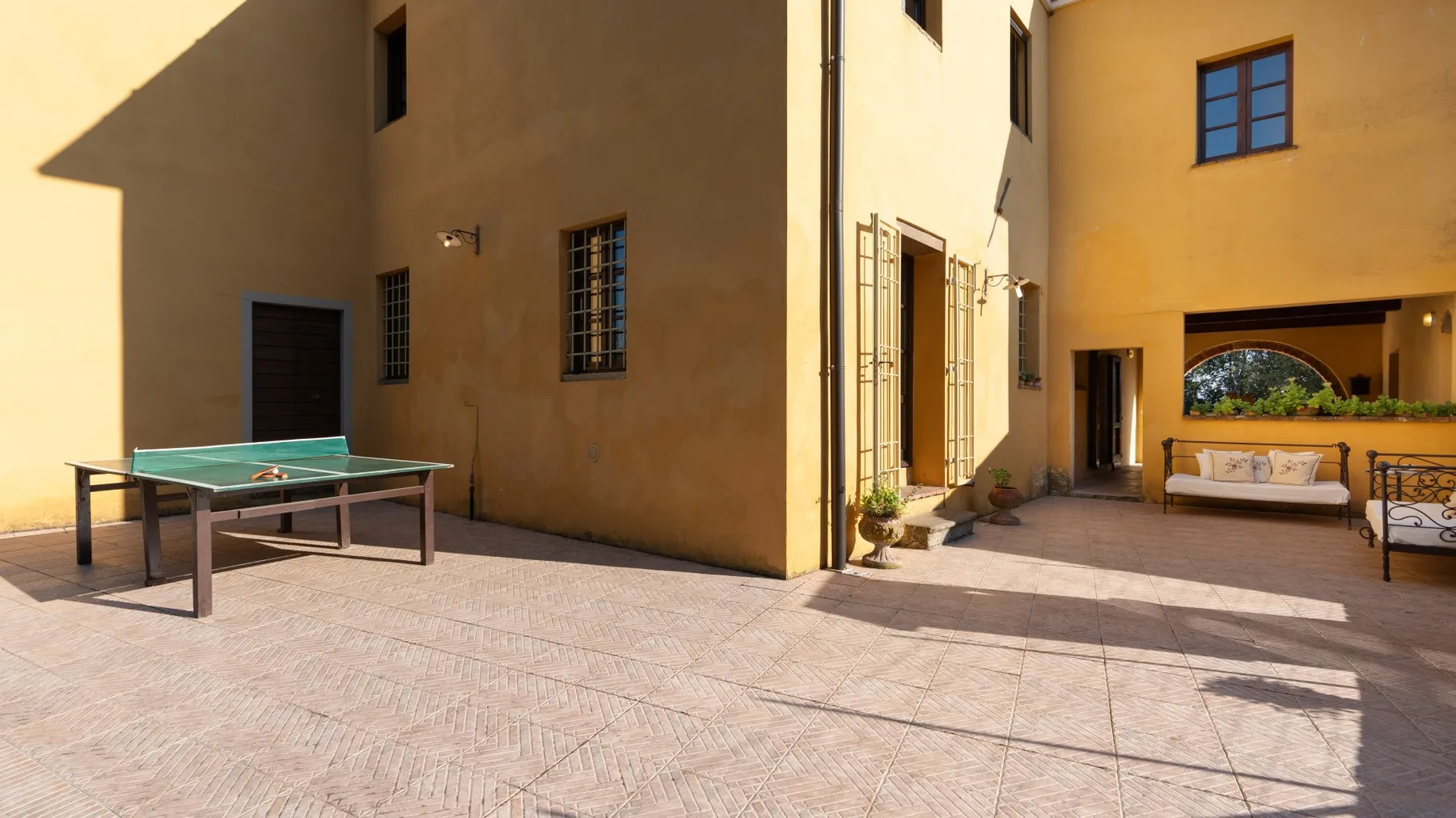 Un patio soleado con una mesa de ping-pong junto a un edificio de tonos cálidos.