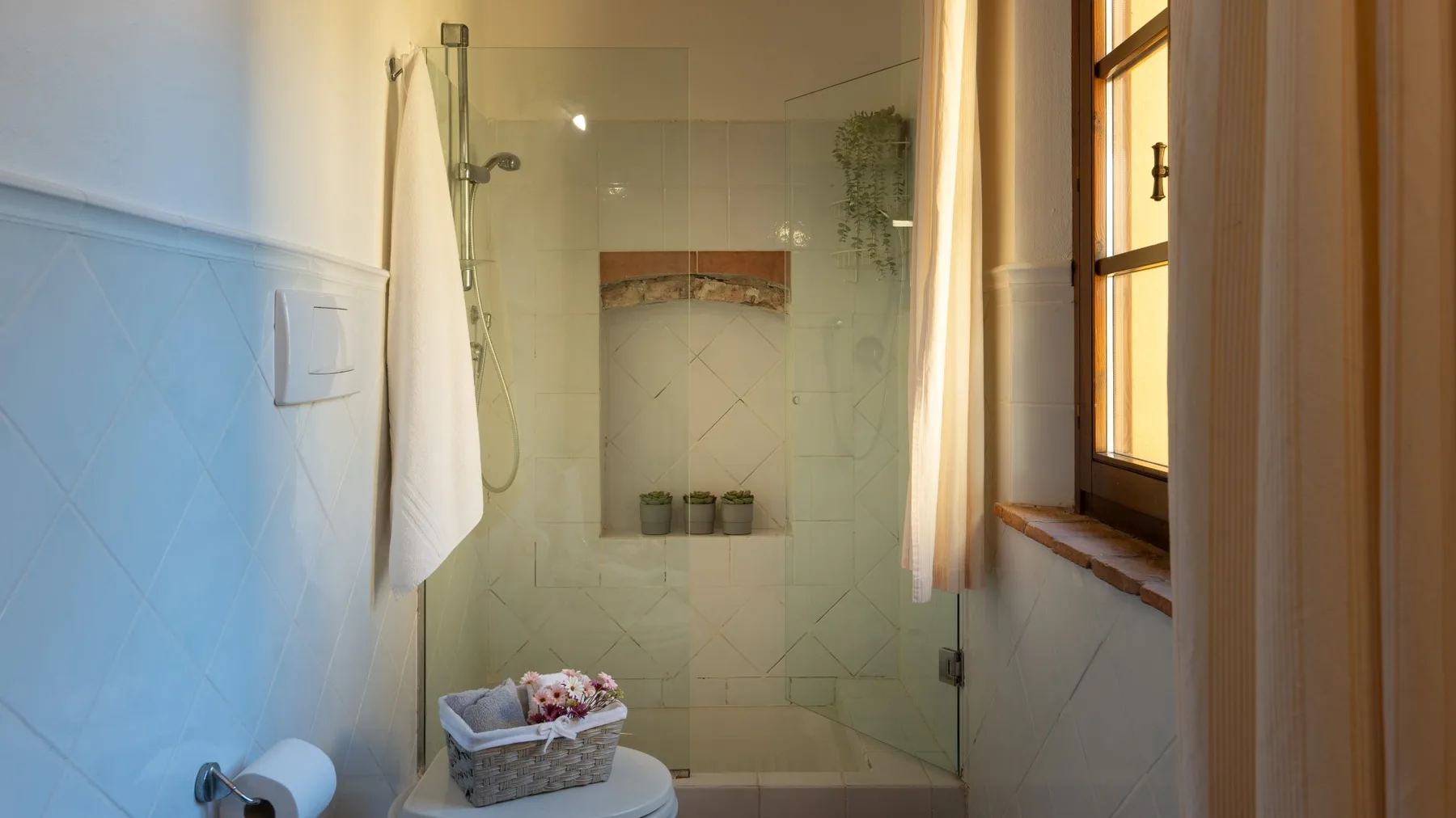 Un baño luminoso con una ducha de vidrio y una ventana al lado.