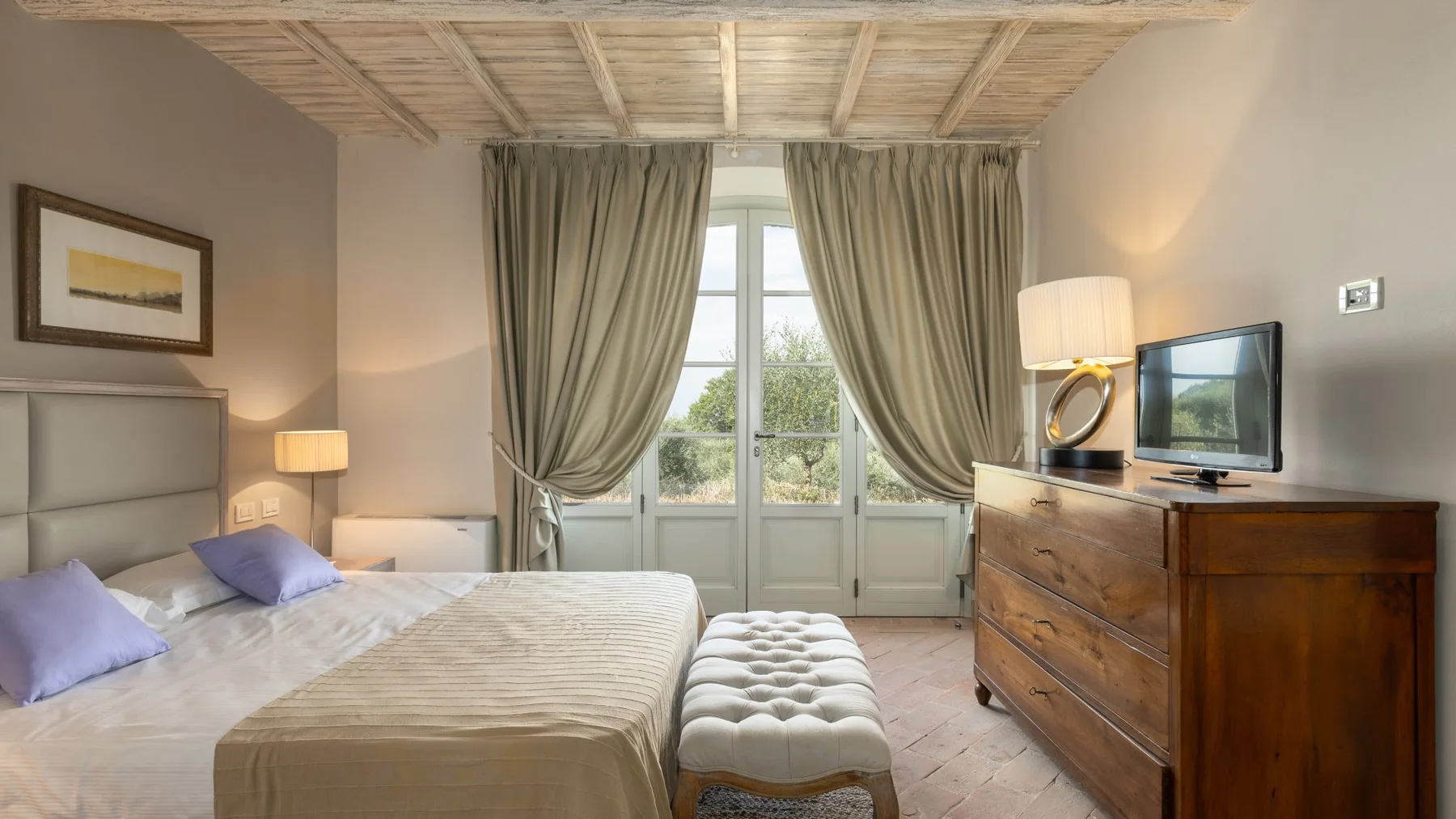 Un dormitorio con una cama, una cómoda de madera y puertas acristaladas con cortinas.