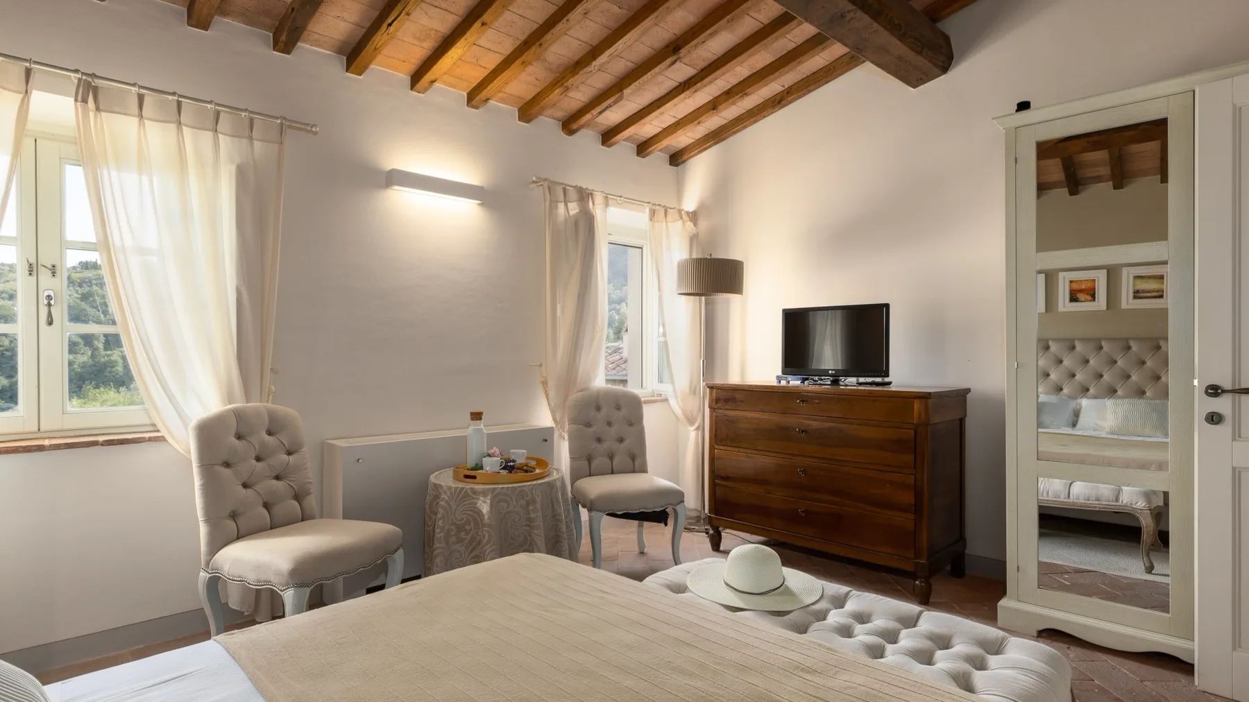 Un dormitorio luminoso con una cama capitoné, dos sillas y una cómoda de madera.