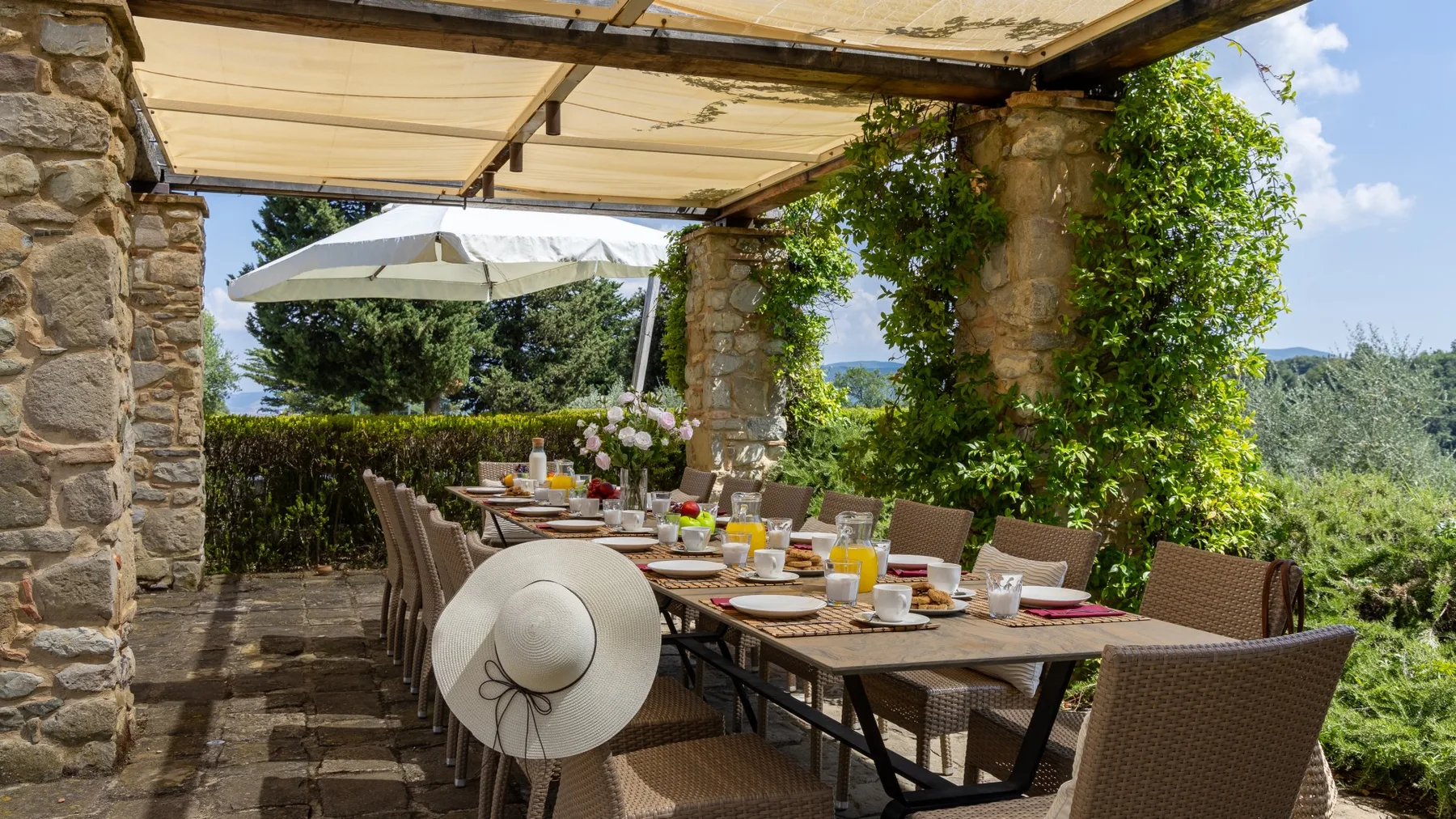 Comedor exterior a la sombra con una mesa larga preparada para comer.