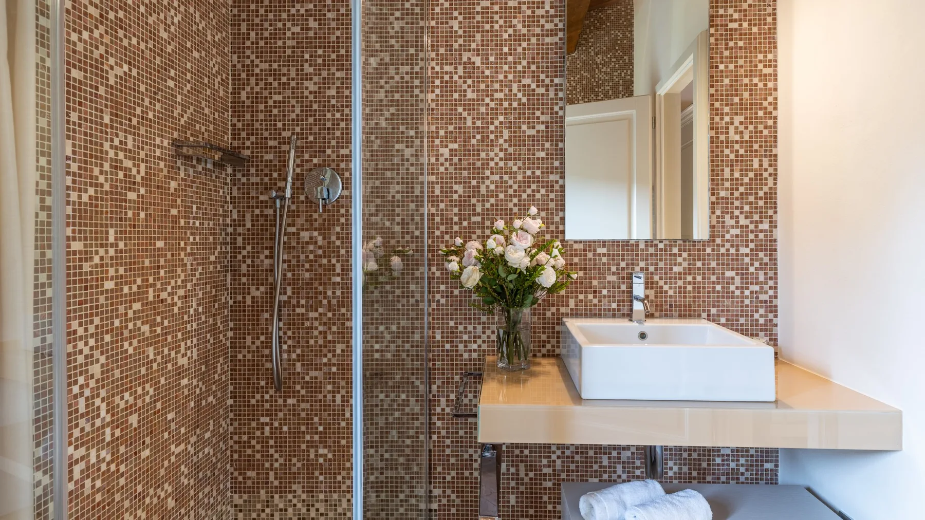 Un baño con ducha de mosaico y un lavabo bajo un espejo.