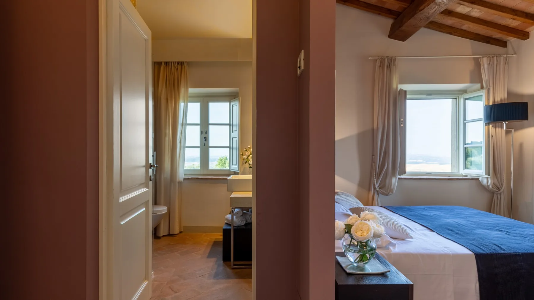 Un dormitorio con una cama cubierta de azul, una ventana abierta y vigas de madera vistas.