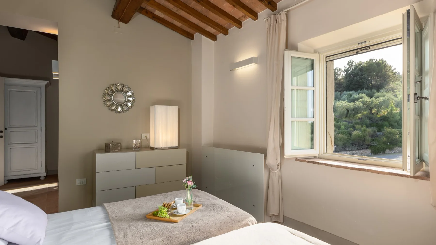 Un dormitorio con una cama bien tendida y ventanas abiertas con vistas a la vegetación.