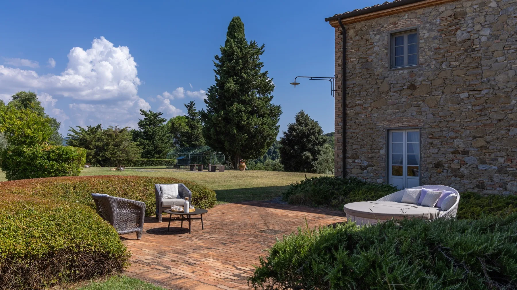 Un patio de ladrillo con asientos al aire libre junto a un edificio de piedra y un jardín.