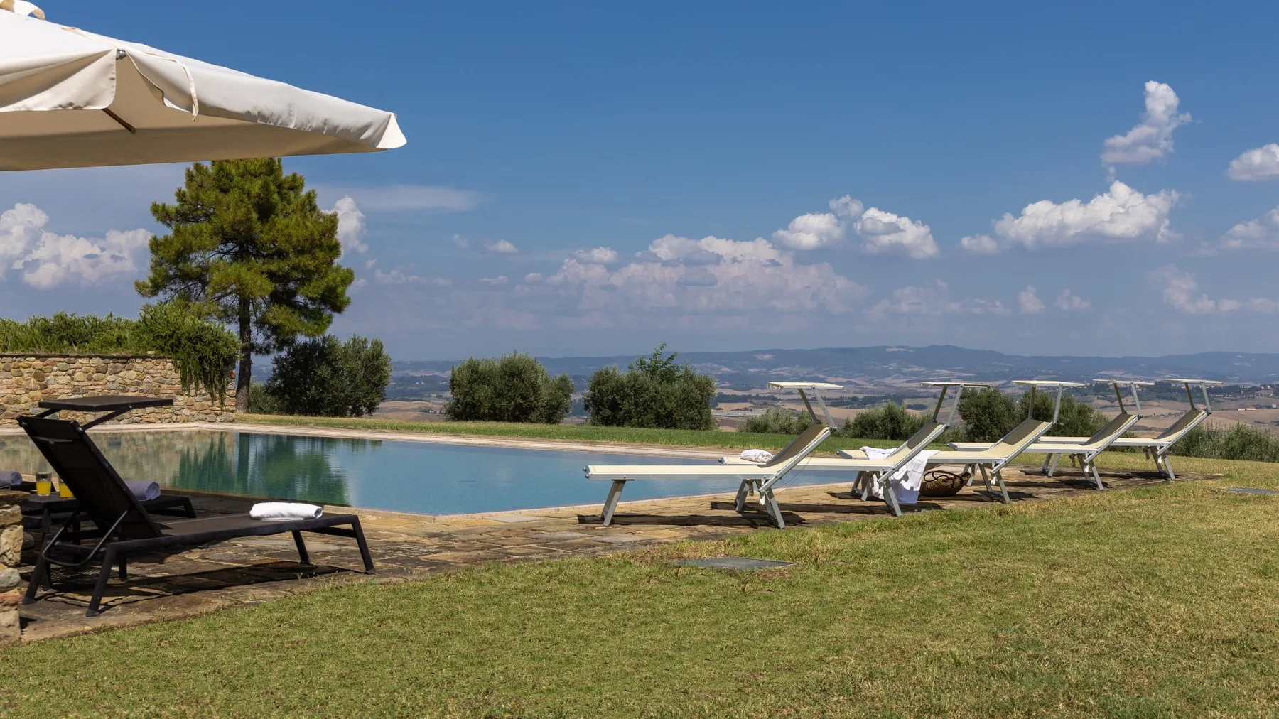 Una piscina al aire libre está junto a un césped y tumbonas reclinables.