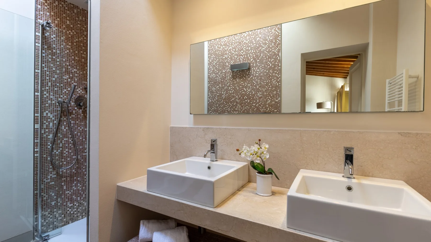Un lavabo de baño con dos lavamanos y una ducha al lado.