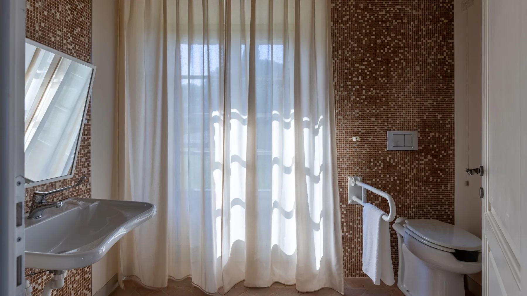 Un baño con lavabo, inodoro y una ventana con cortinas.