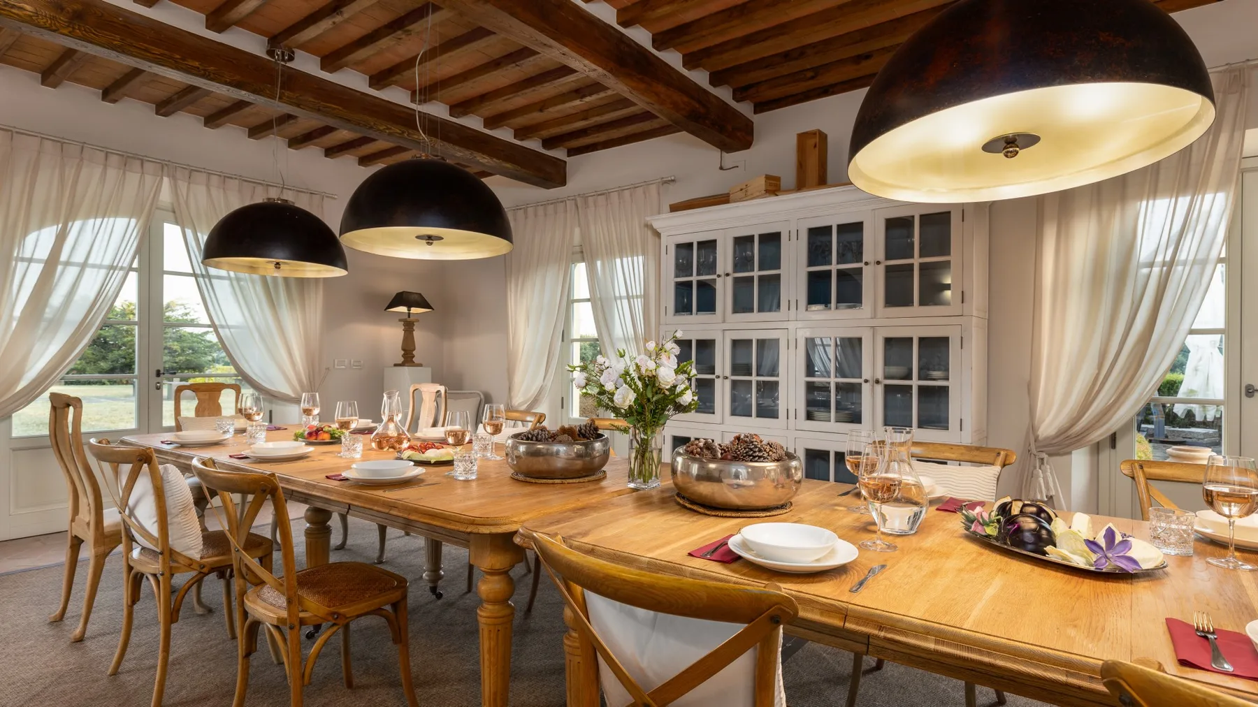 Un comedor con una larga mesa de madera puesta con vajilla bajo lámparas colgantes.