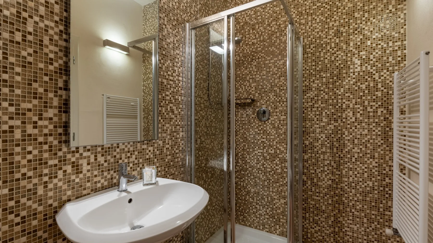 Un baño alicatado con lavabo y ducha con mampara de vidrio.