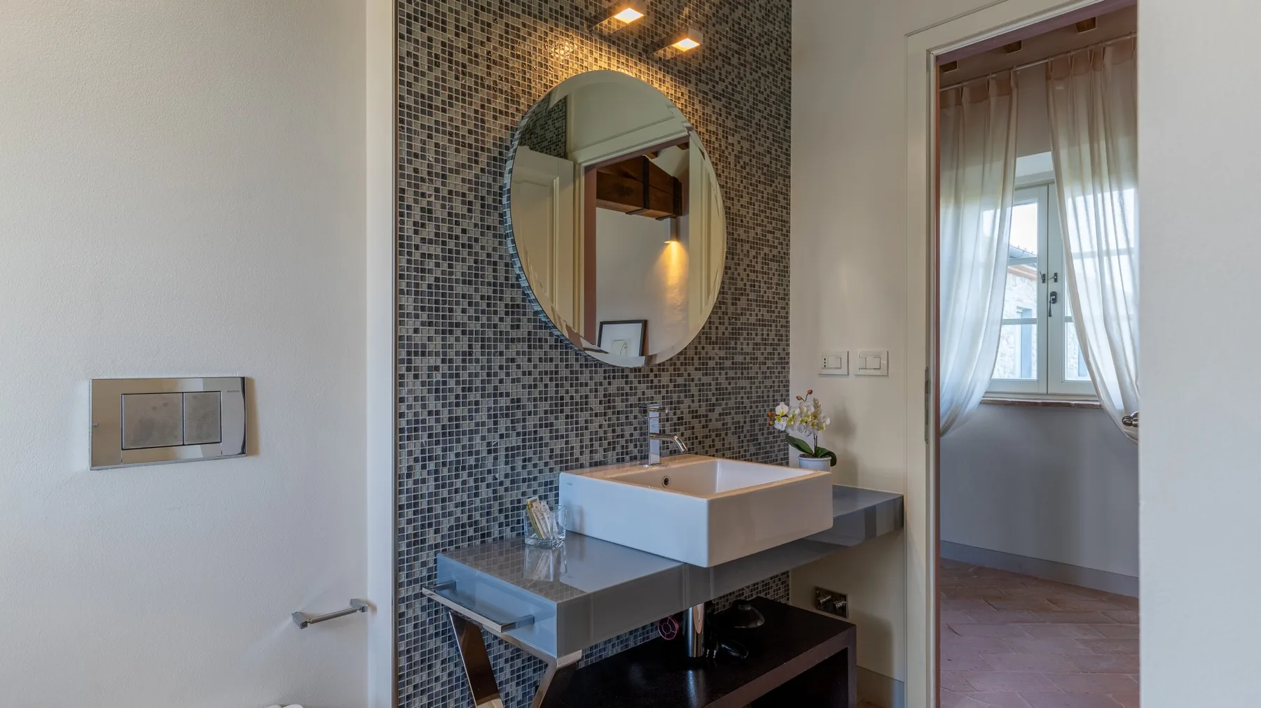 Un lavabo de baño con un fregadero rectangular está debajo de un espejo redondo.