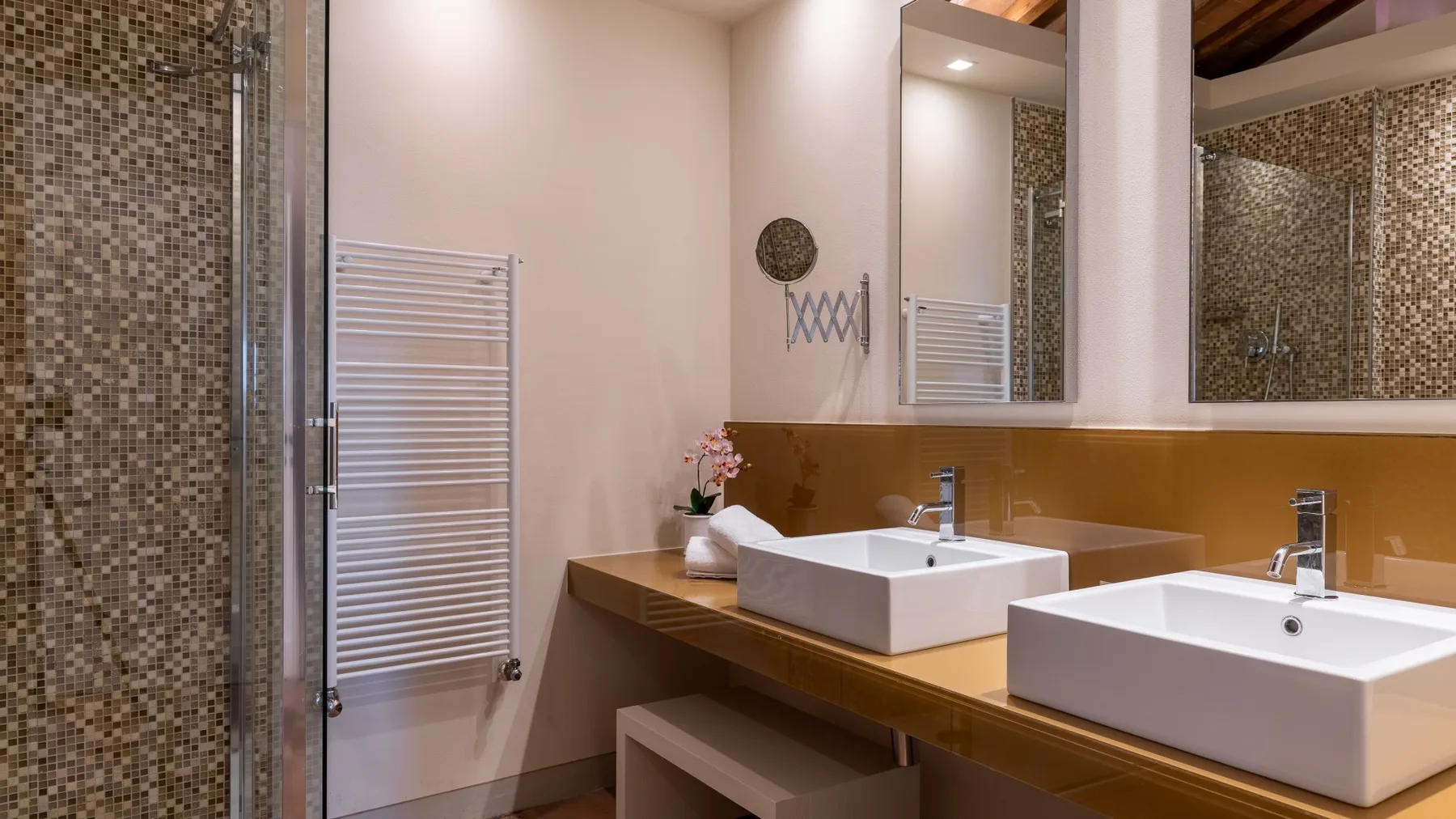 Un baño con dos lavabos sobre encimera, espejos de pared y una ducha con azulejos.