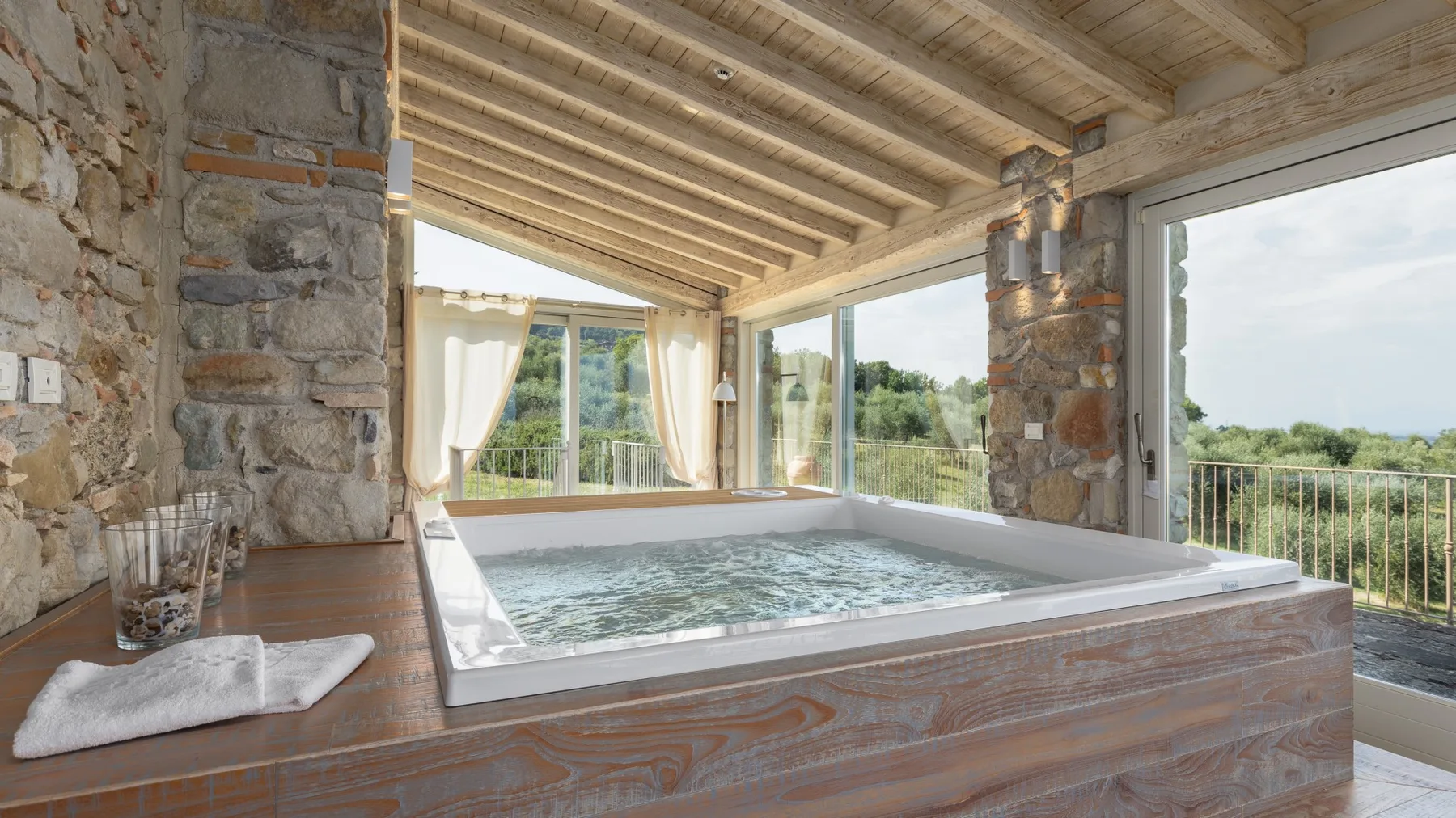 Una piscina cubierta tipo spa está junto a grandes ventanales con vistas a zonas verdes.