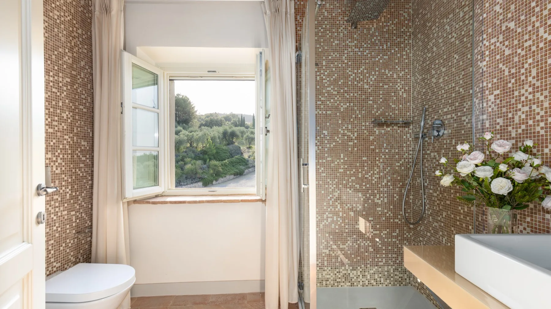 Un baño alicatado con bañera, inodoro y una ventana abierta con vistas a la vegetación.