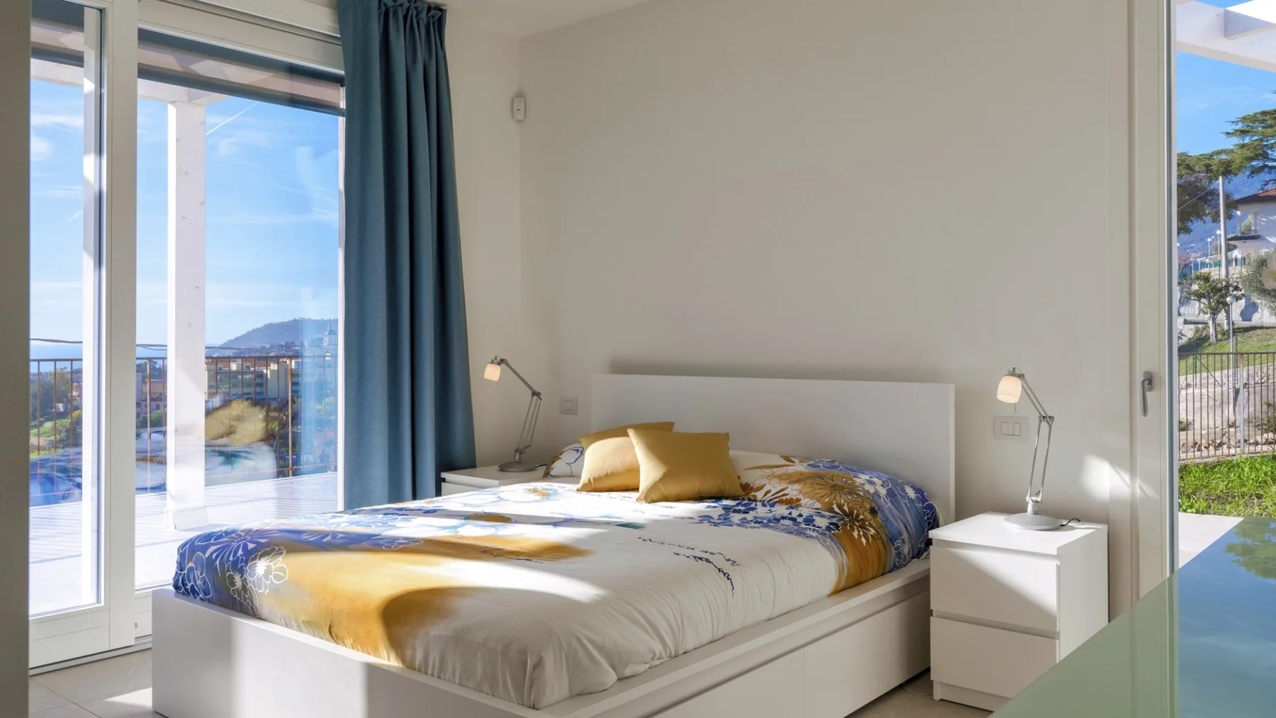 Un dormitorio luminoso con una cama junto a grandes ventanas y cortinas azules.
