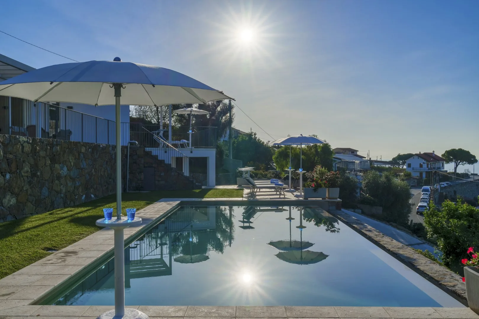 Una piscina al aire libre refleja el sol junto a una zona de estar con sombra.