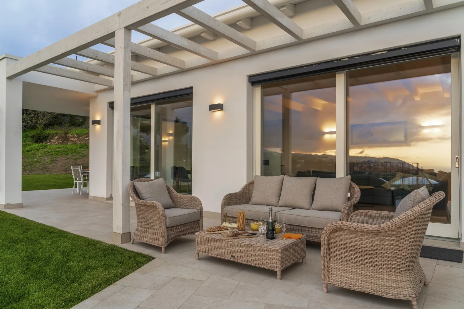 Una zona de estar al aire libre está junto a grandes puertas de vidrio bajo una pérgola.