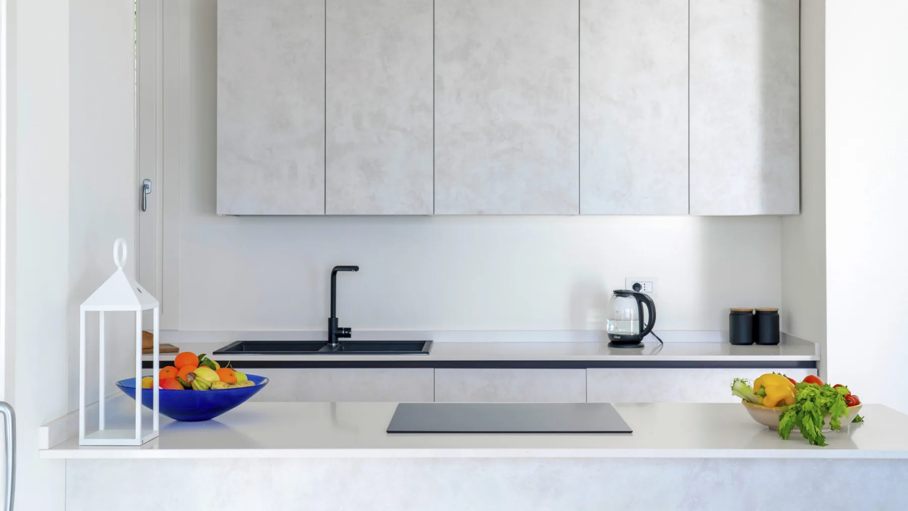 Una cocina moderna con una encimera larga, armarios superiores y fruta sobre la superficie.