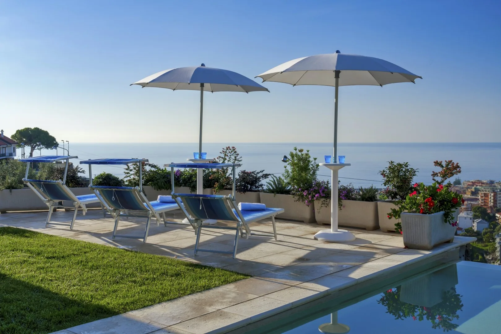 Una terraza soleada junto a la piscina da al mar, con asientos reclinables y sombrillas.