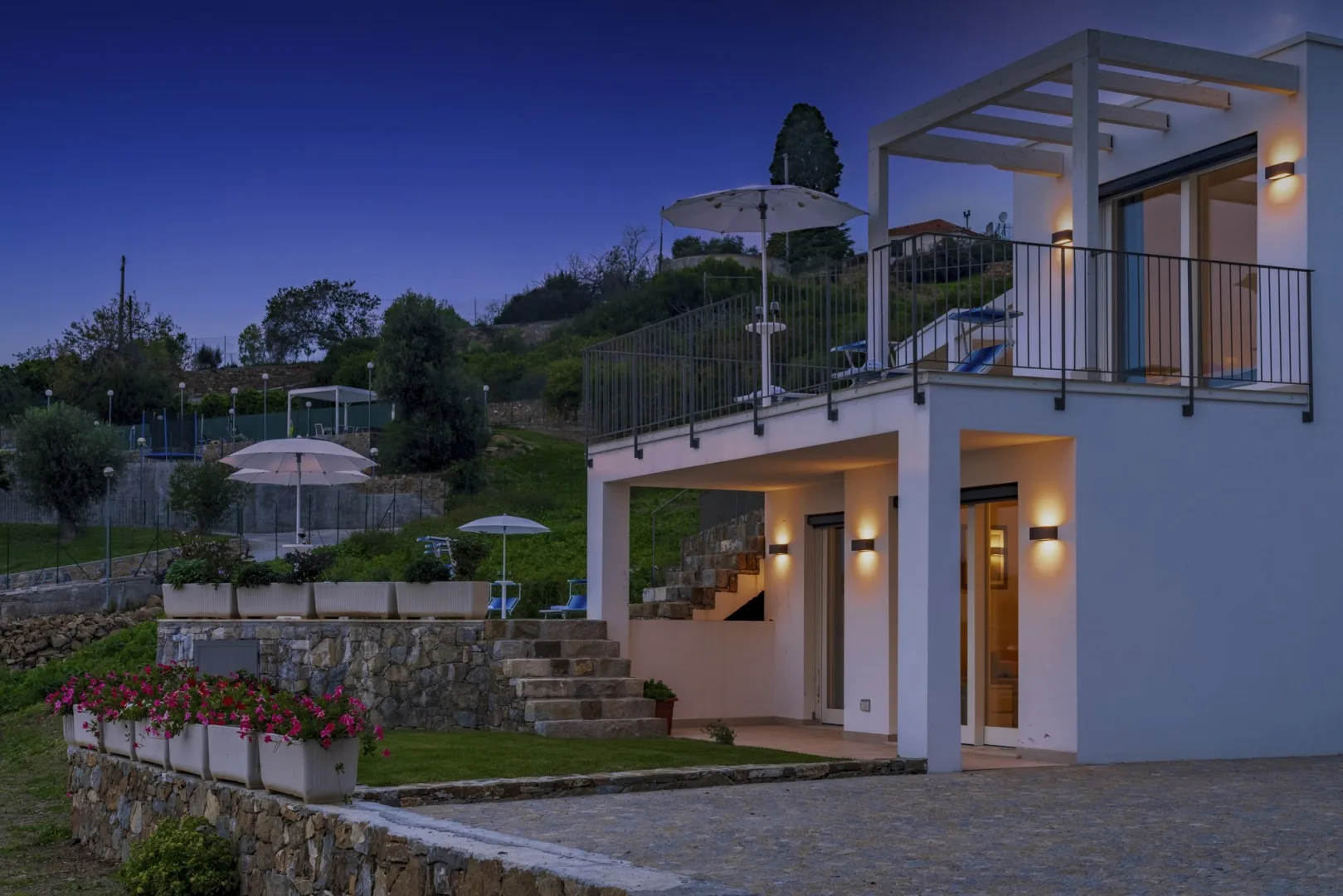 Una casa moderna en la ladera se abre a una terraza iluminada con asientos en el jardín.