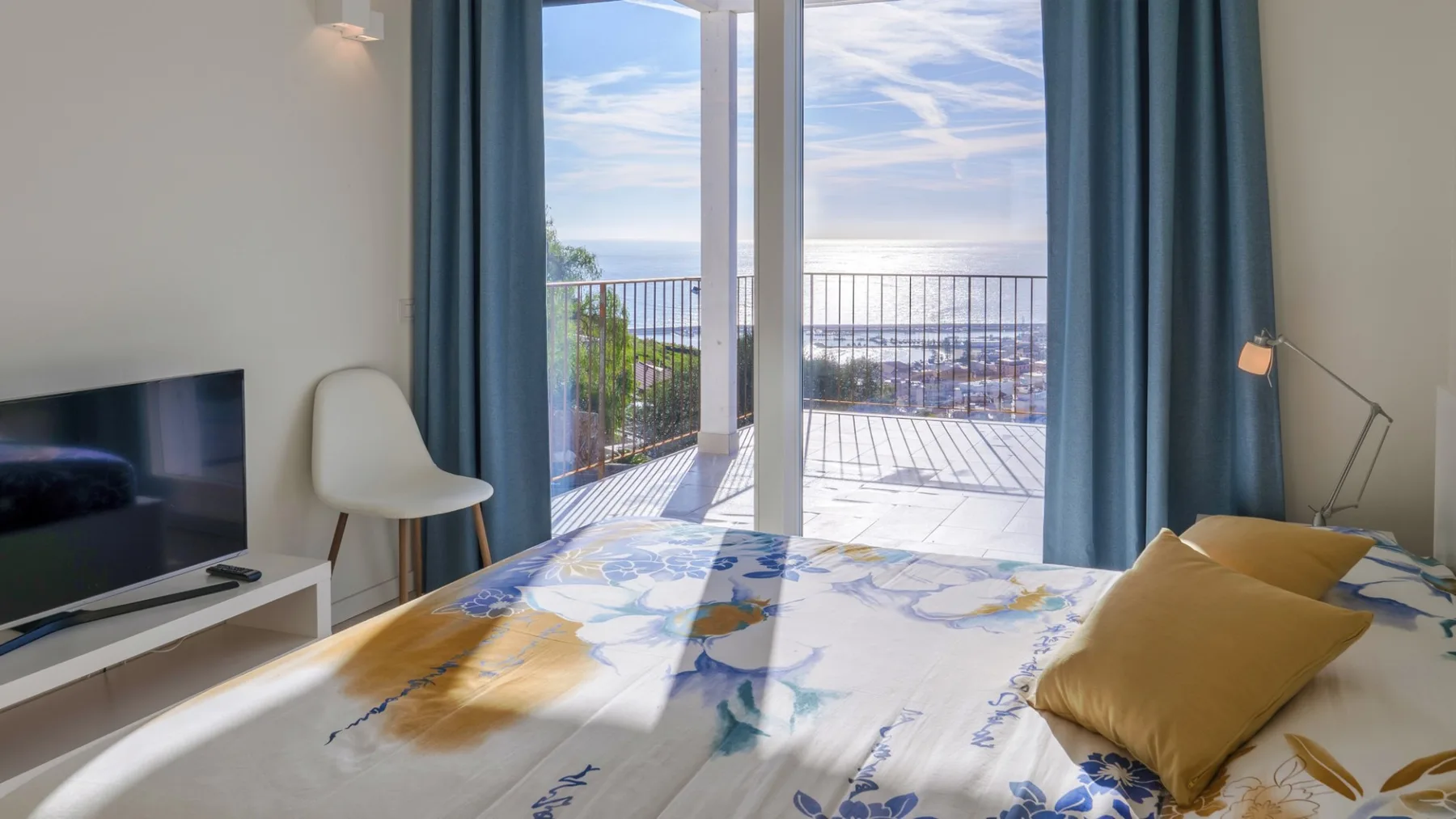 Un dormitorio con una cama junto a puertas de vidrio abiertas que dan a un balcón.