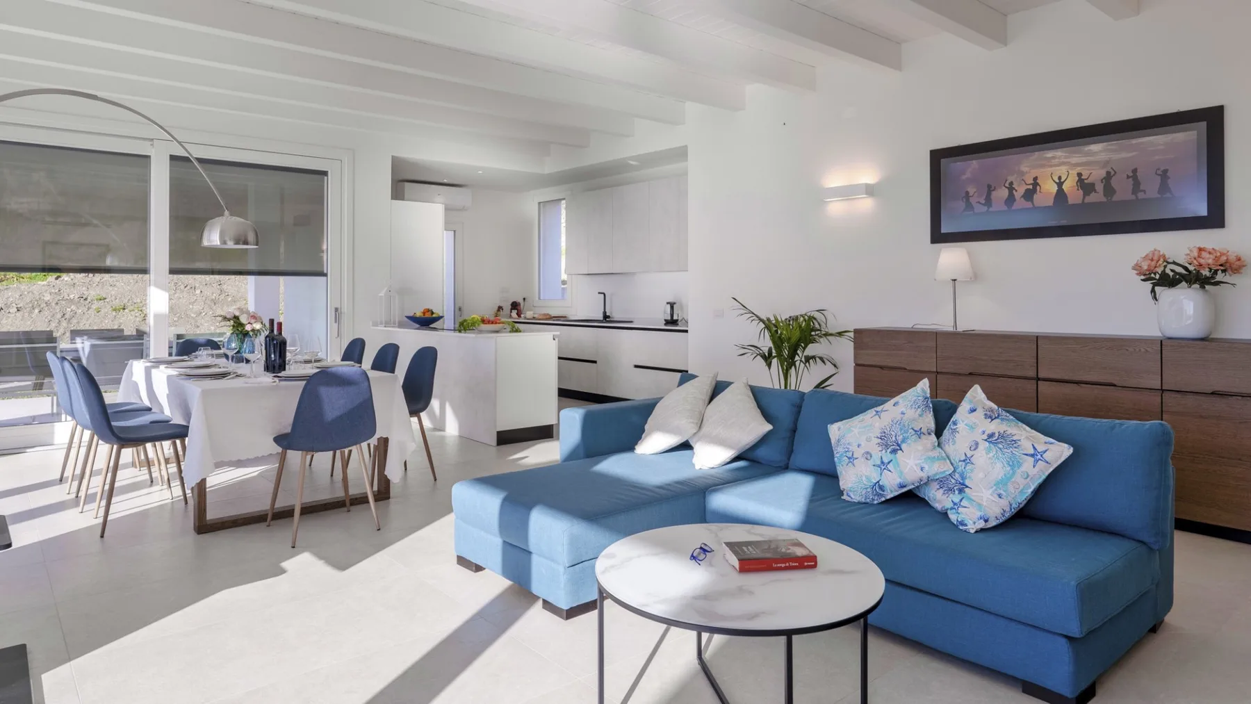 Una luminosa sala de estar y comedor de planta abierta, con asientos azules y una mesa blanca.