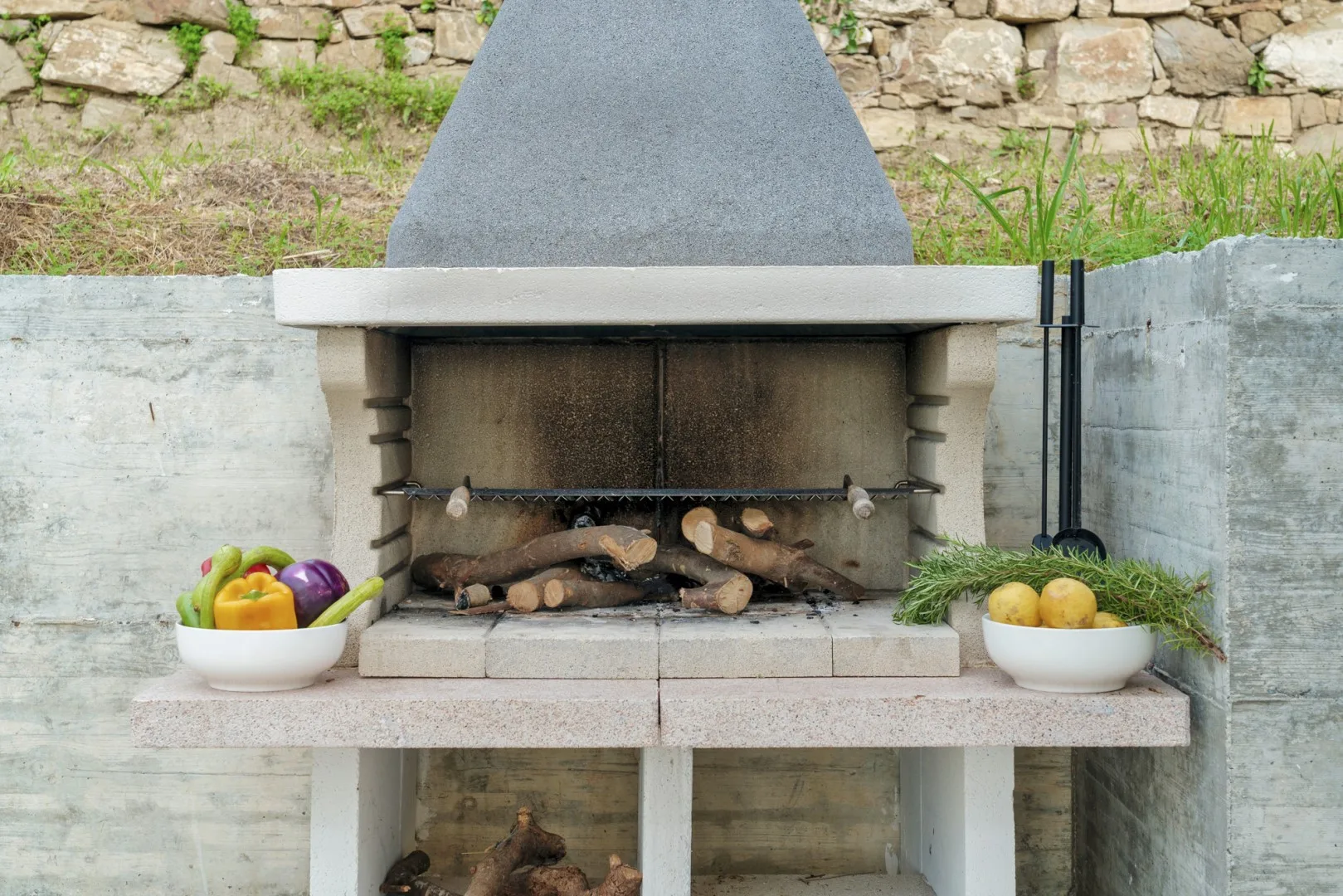 Una zona de barbacoa de piedra al aire libre con leña y cuencos de productos.