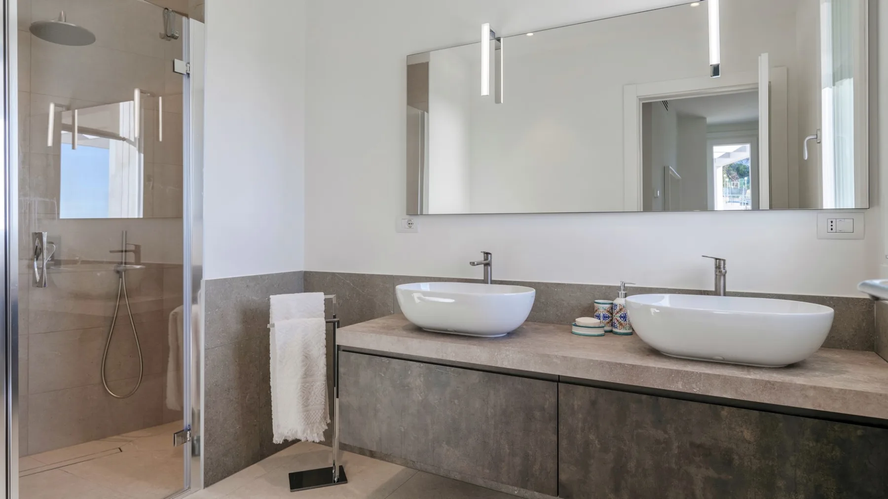 Un baño moderno con tocador de doble lavabo y una ducha con mampara de vidrio.