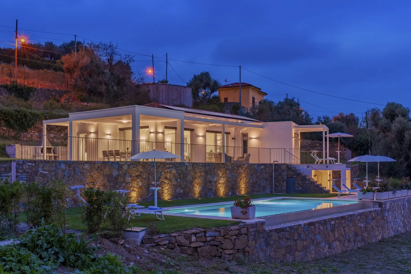 Una casa moderna con patio iluminado y piscina al anochecer.