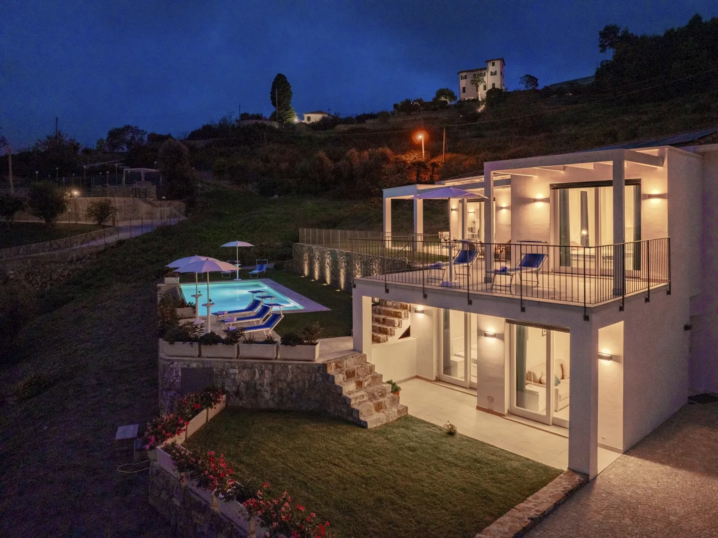 Una casa moderna al anochecer domina una piscina iluminada y jardines.