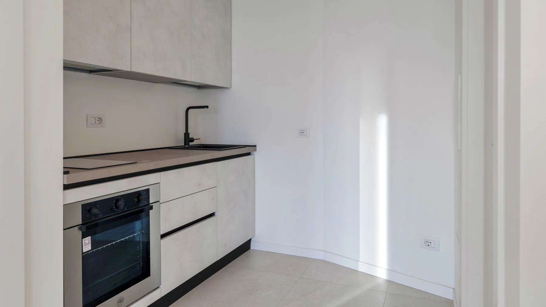 Una cocina compacta con armarios claros, una encimera oscura y un horno integrado.