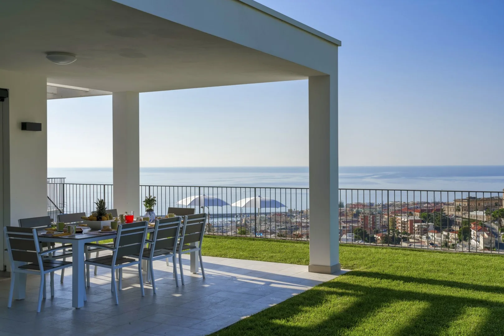 Una zona de comedor exterior cubierta ofrece vistas a un pueblo costero y al mar.