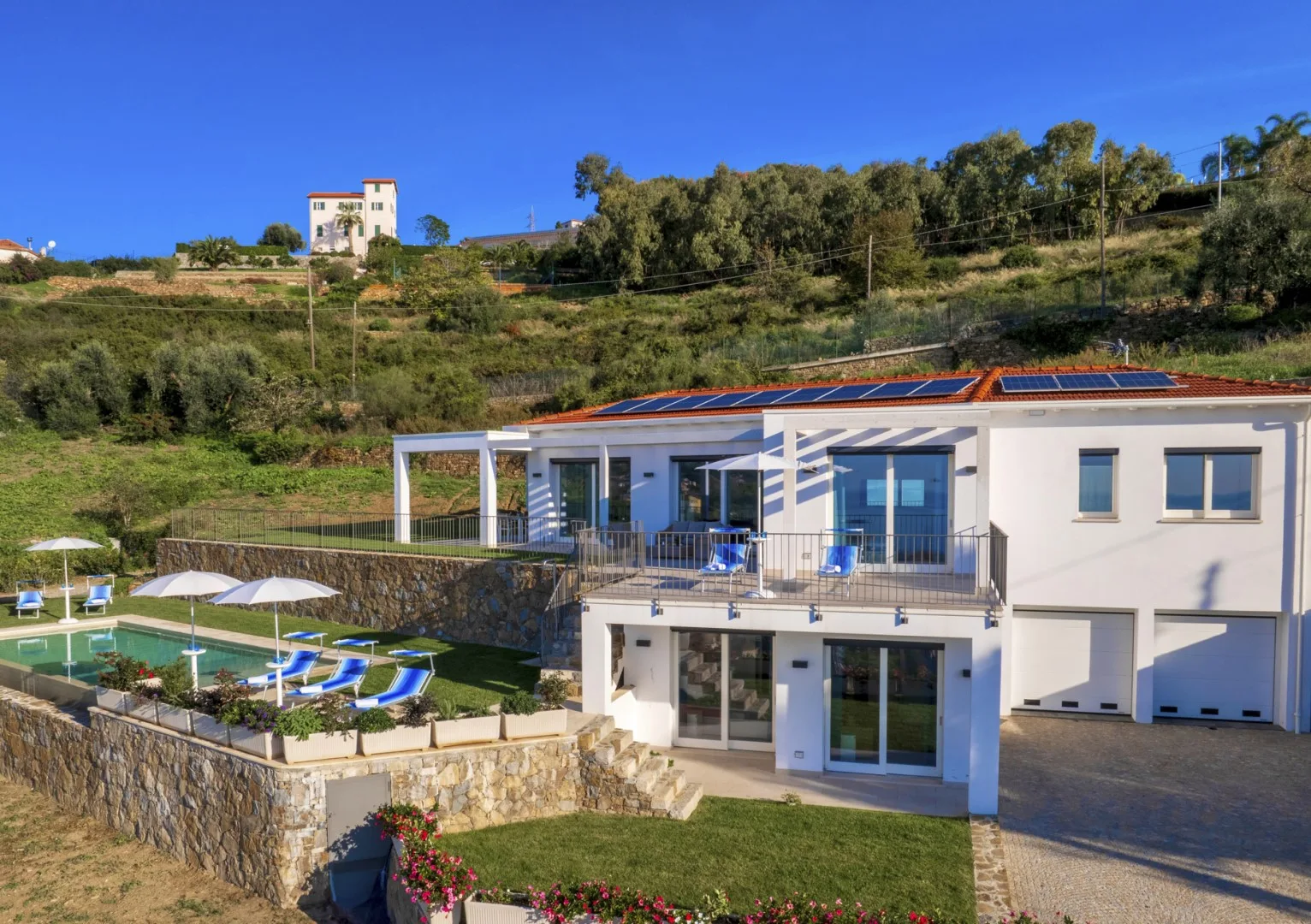Una casa moderna con piscina y jardines se encuentra al pie de una colina.