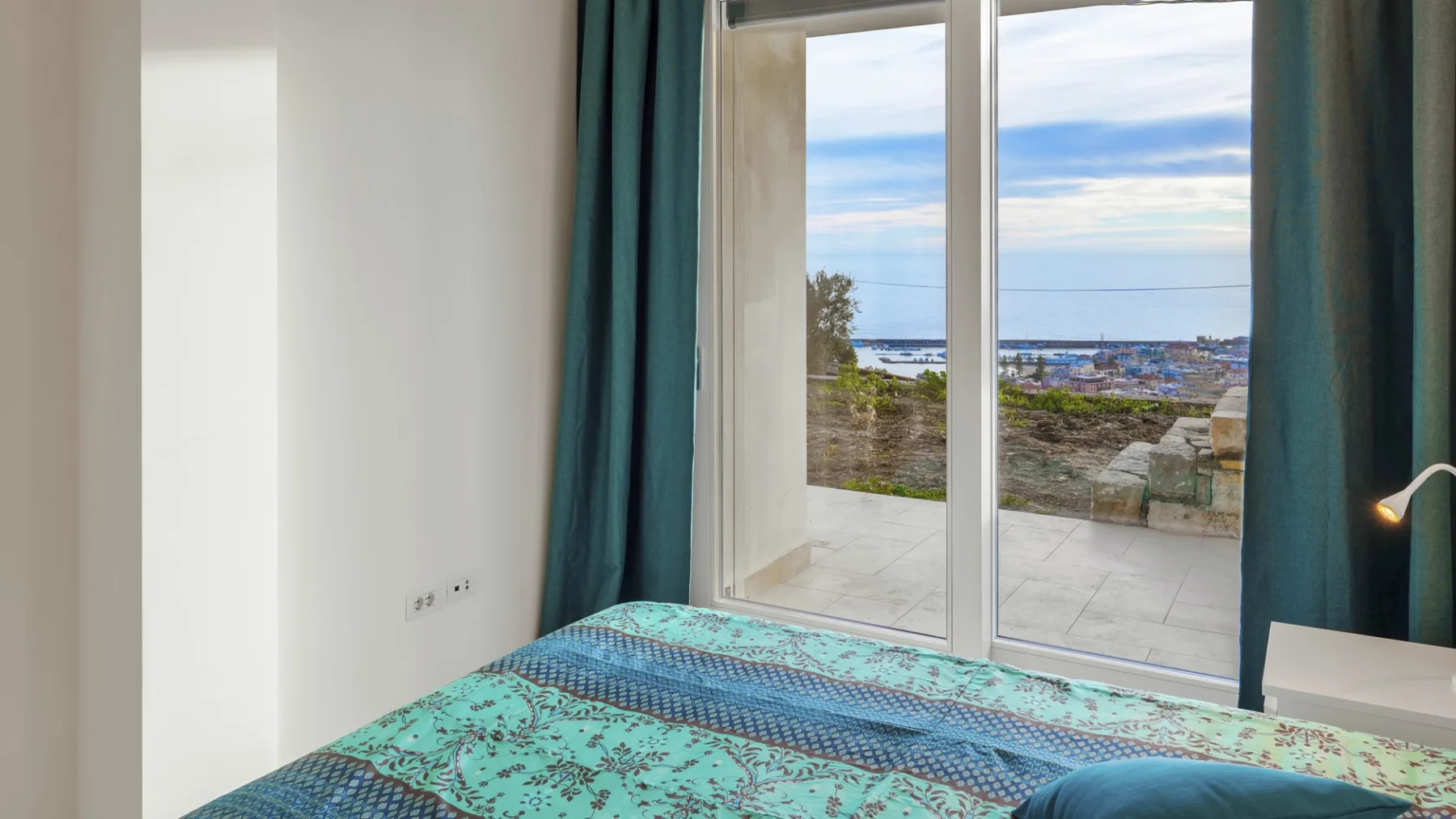 Un dormitorio con una cama junto a puertas de vidrio con vistas a la costa.
