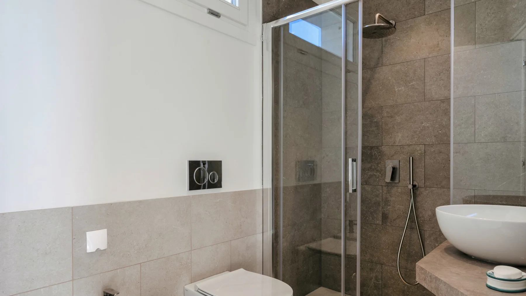 Un baño con azulejos, una ducha de vidrio y un lavabo sobre encimera.