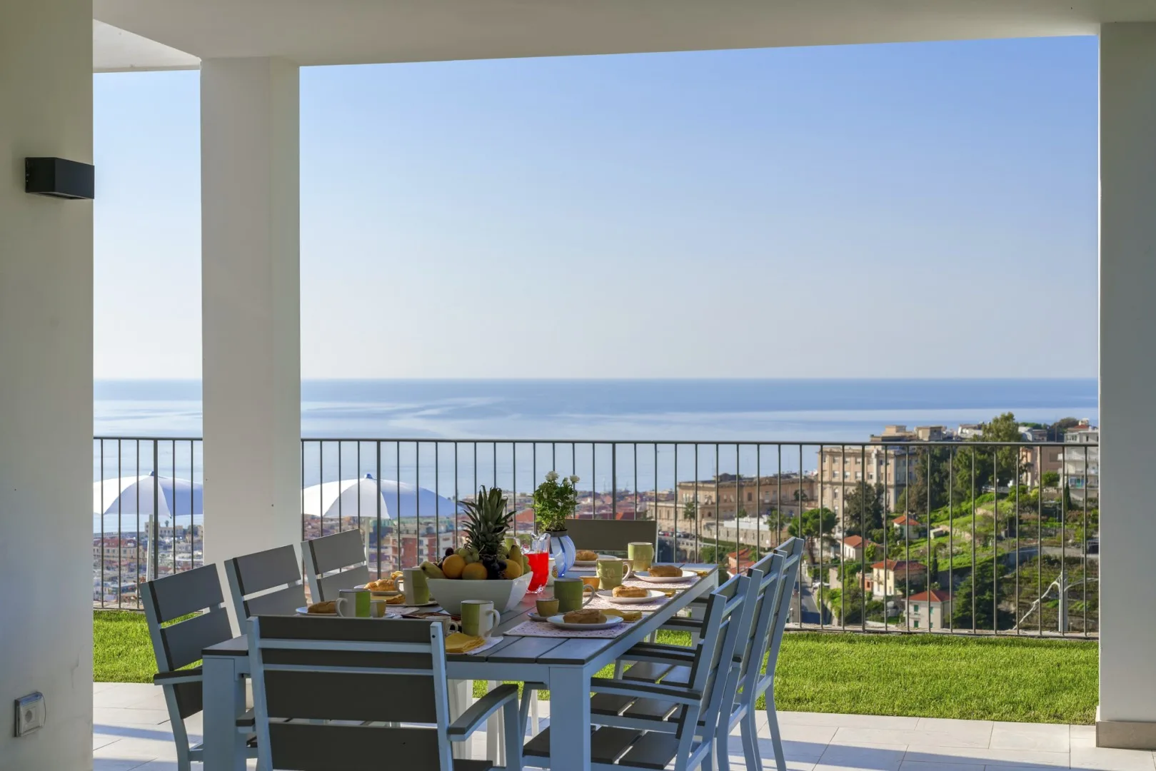 Una zona de comedor en un patio cubierto mira al mar y a edificios cercanos.