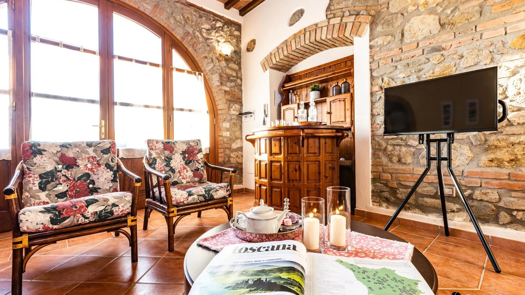 A rustic living area with floral seating, a wooden bar, and a television.
