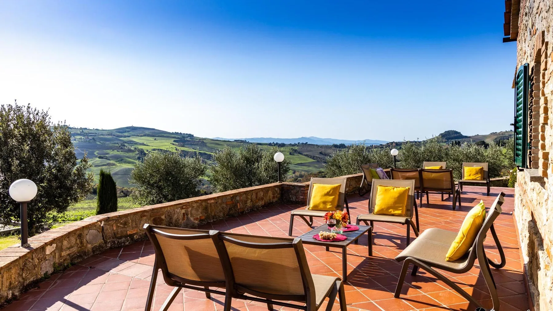 An outdoor terrace with seating and yellow cushions overlooks a green countryside landscape.