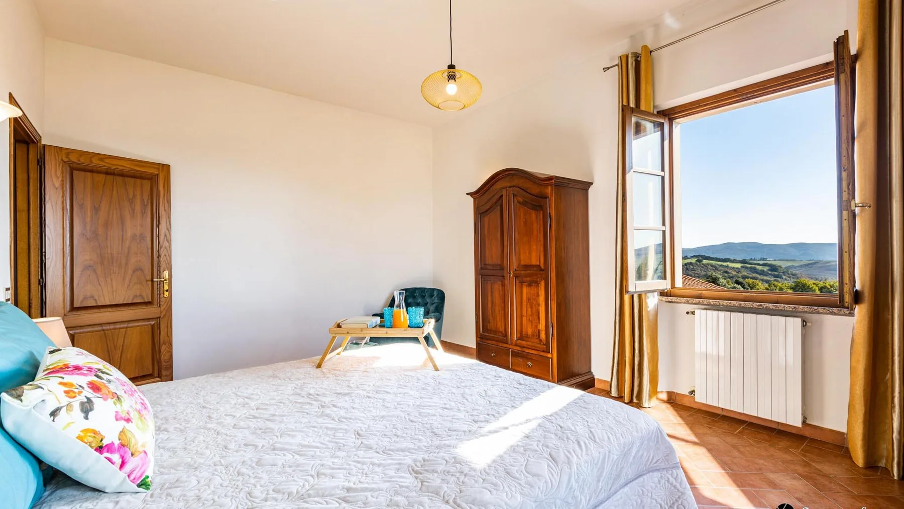 A bedroom with a large bed, wooden wardrobe, and a window overlooking hills.
