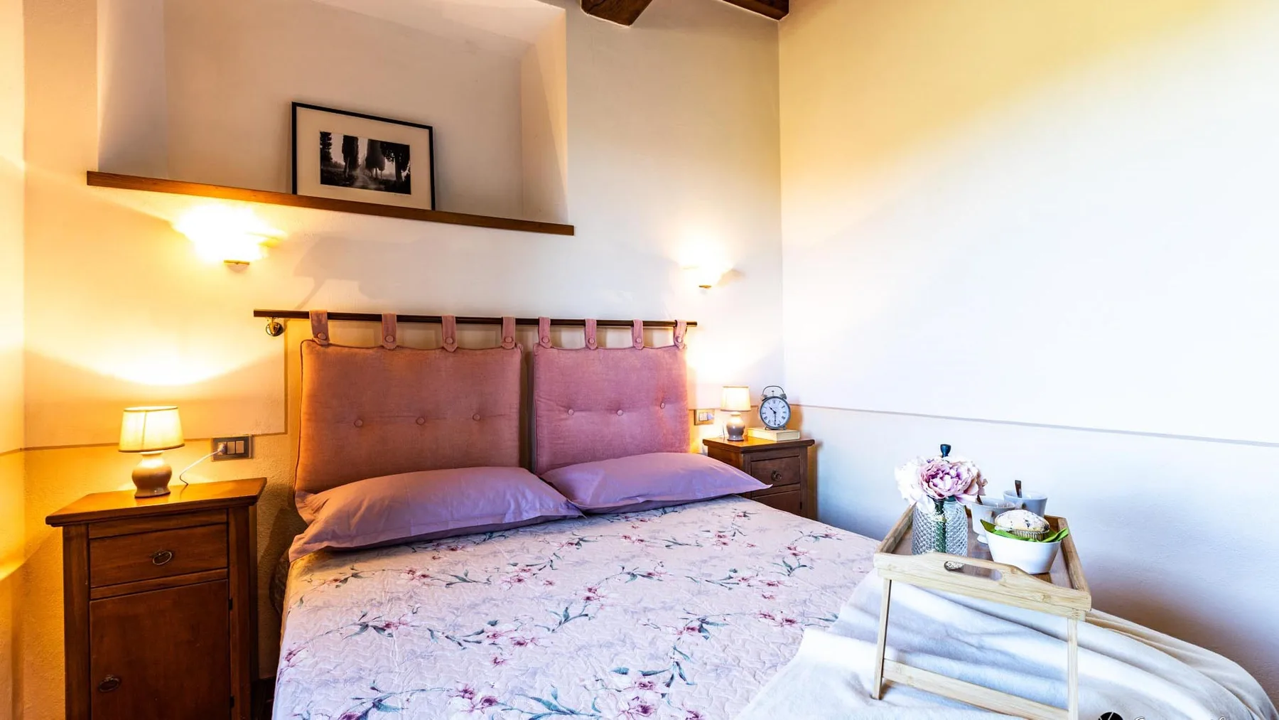 A bedroom with a bed, bedside tables, and a framed picture on a wall shelf.