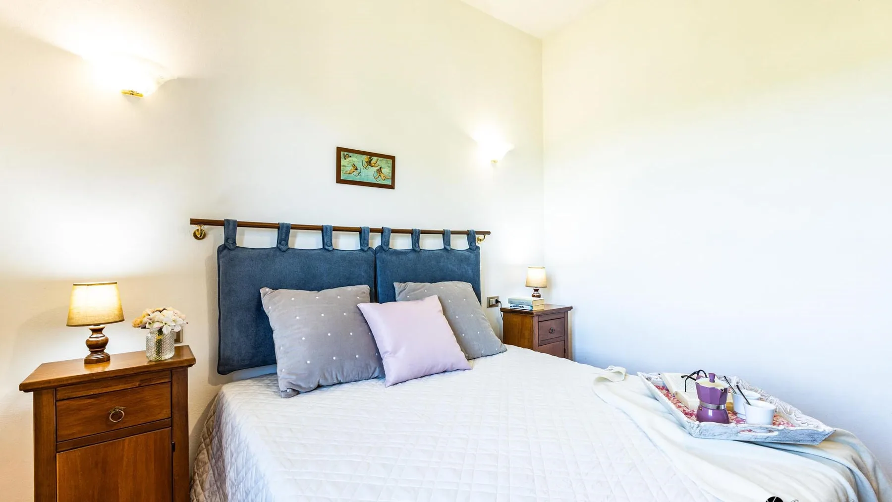 A bedroom with a large bed, bedside tables, and wall lights.