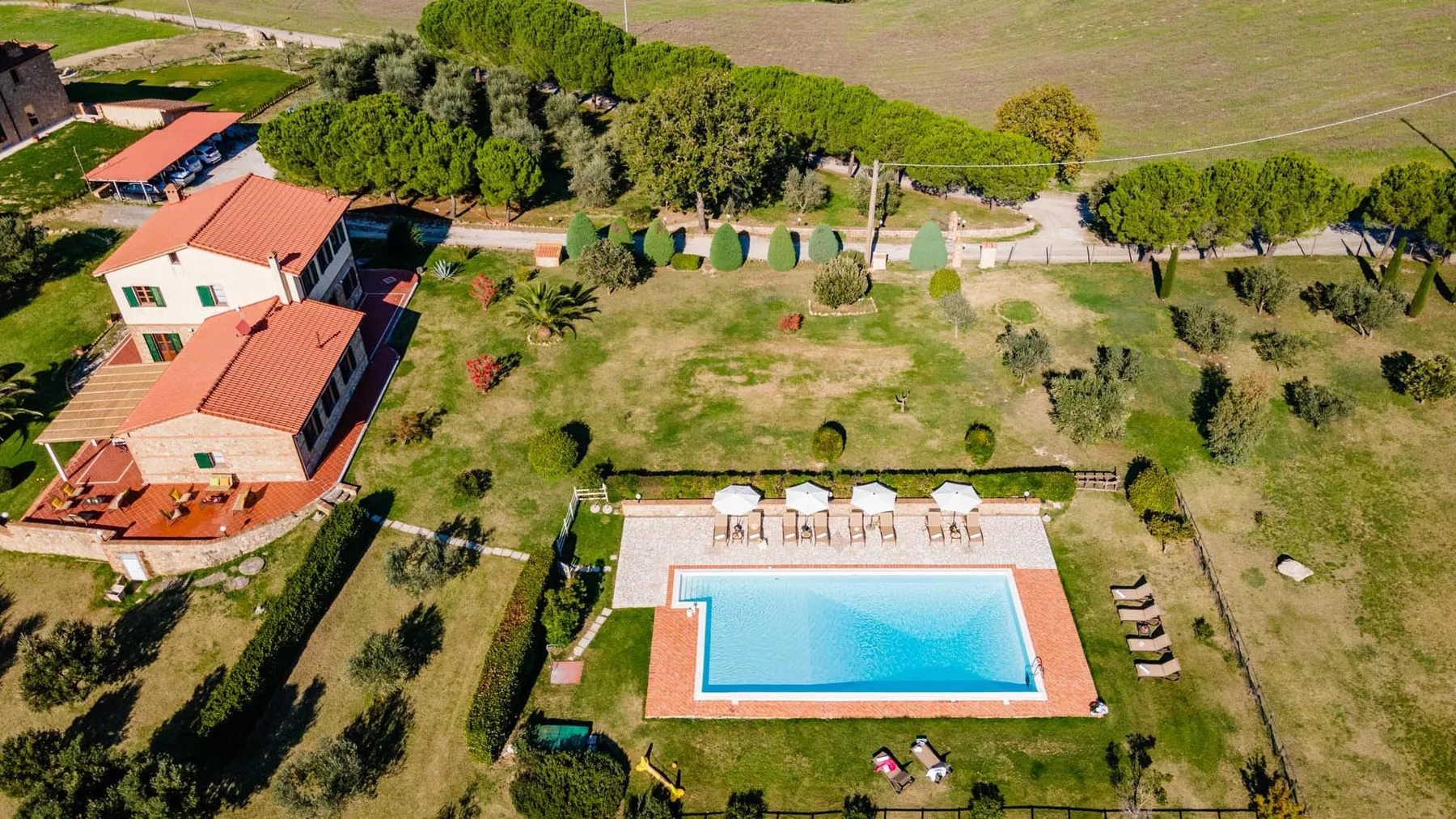 Aerial view of a swimming pool beside a house, surrounded by landscaped grounds.