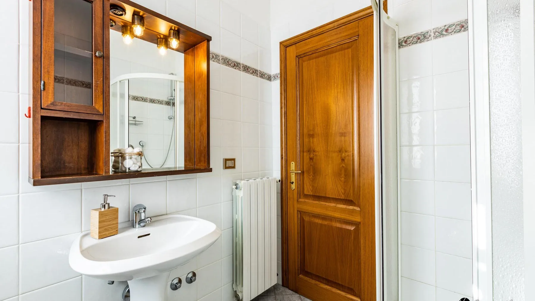 A tiled bathroom with a sink, mirror cabinet, and wooden door.