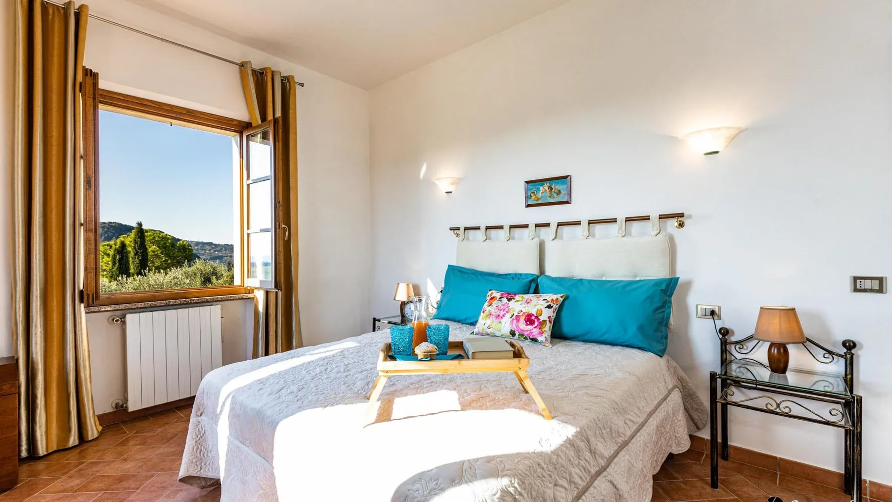 A bedroom with a double bed, turquoise pillows, and a large open window.