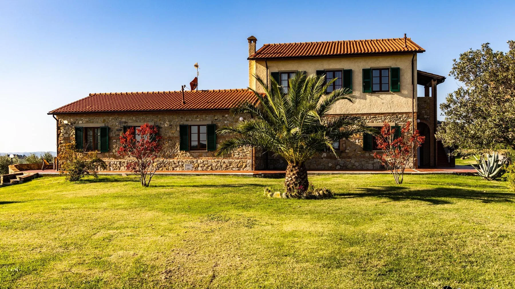 A country house with a tiled roof stands beyond a broad green lawn.