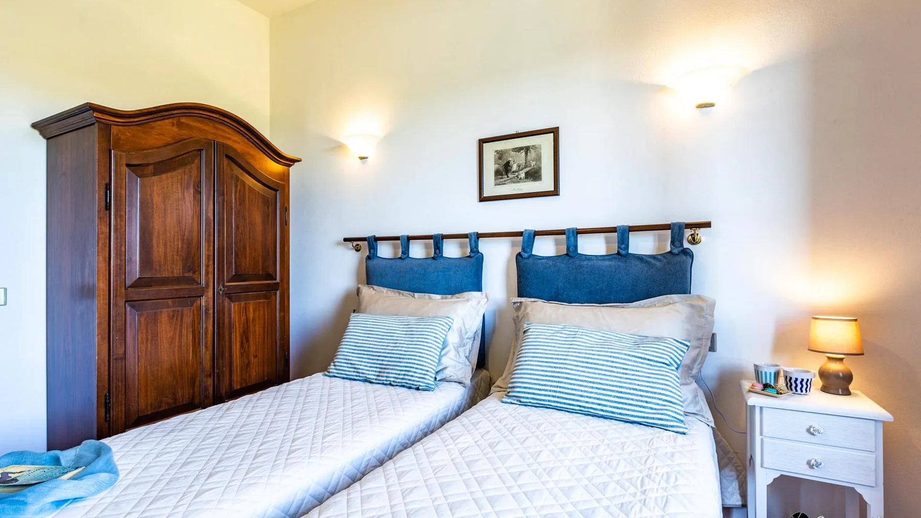 A twin bedroom with two beds, blue headboards, and a wooden wardrobe.
