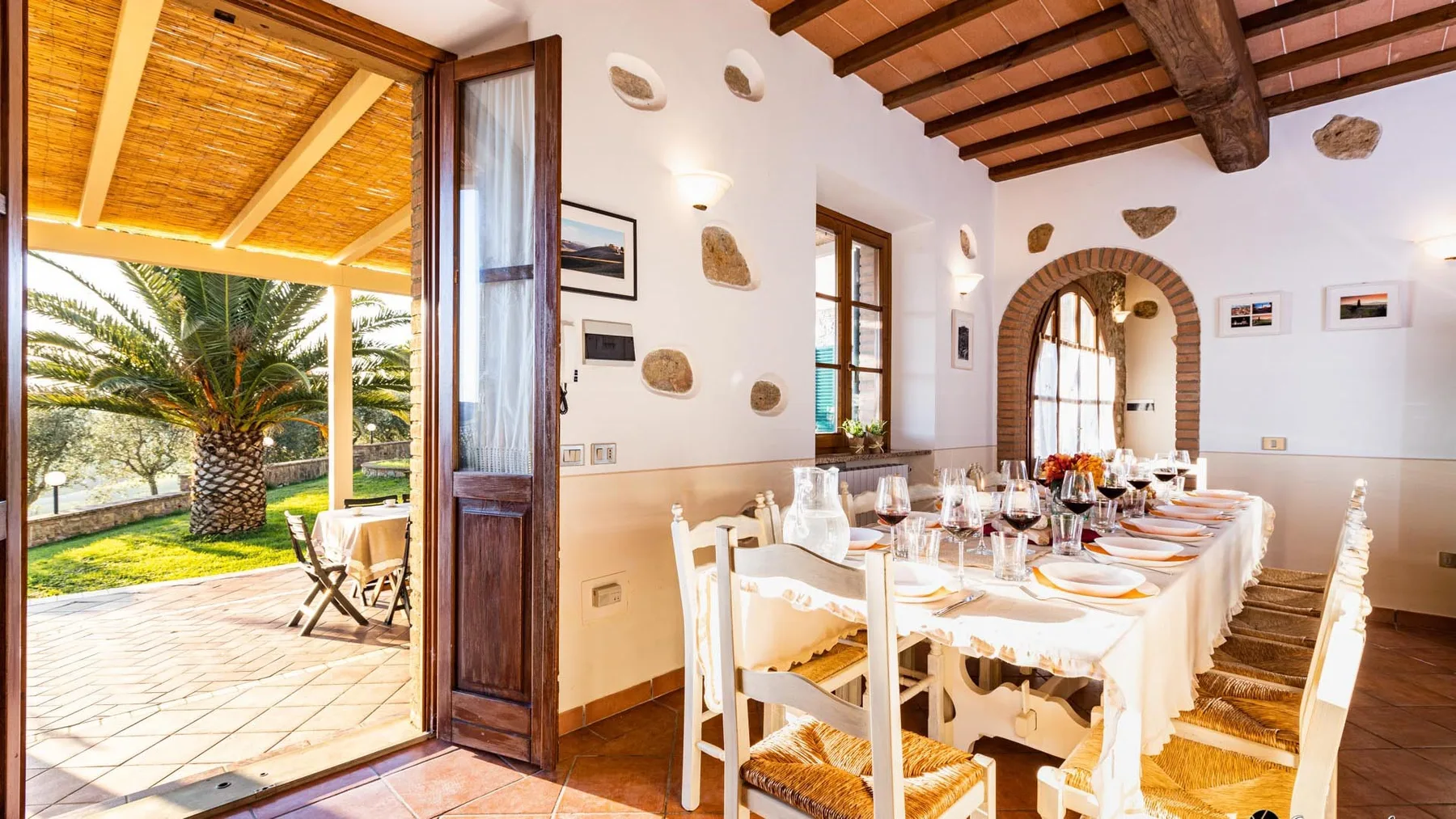 A dining room with a long set table beside open doors to a sunlit patio.
