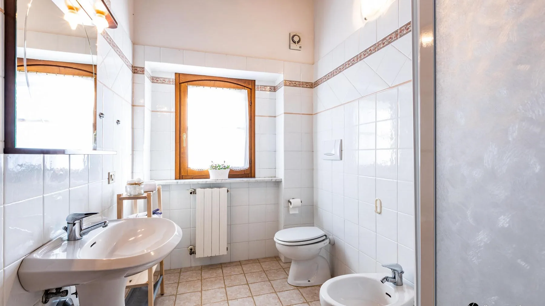 A tiled bathroom with a sink, toilet, and window.