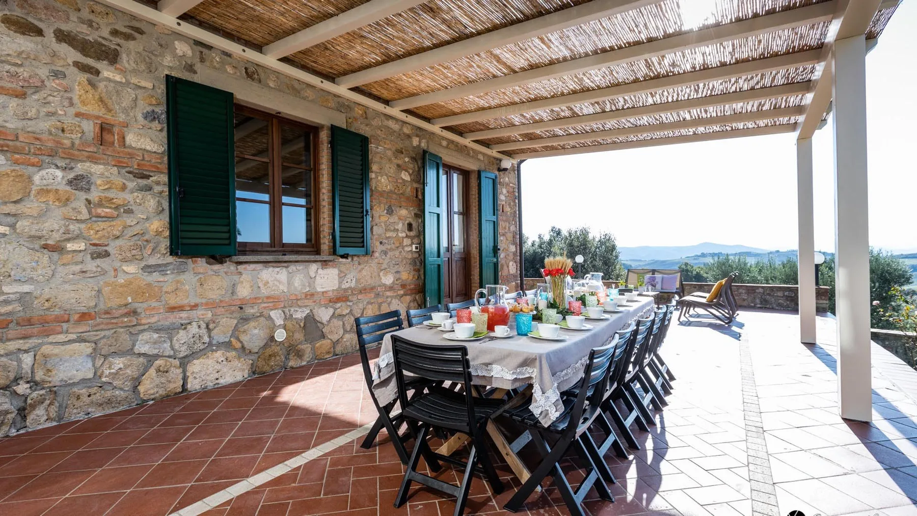 A covered outdoor dining area with a long table beside a stone wall.